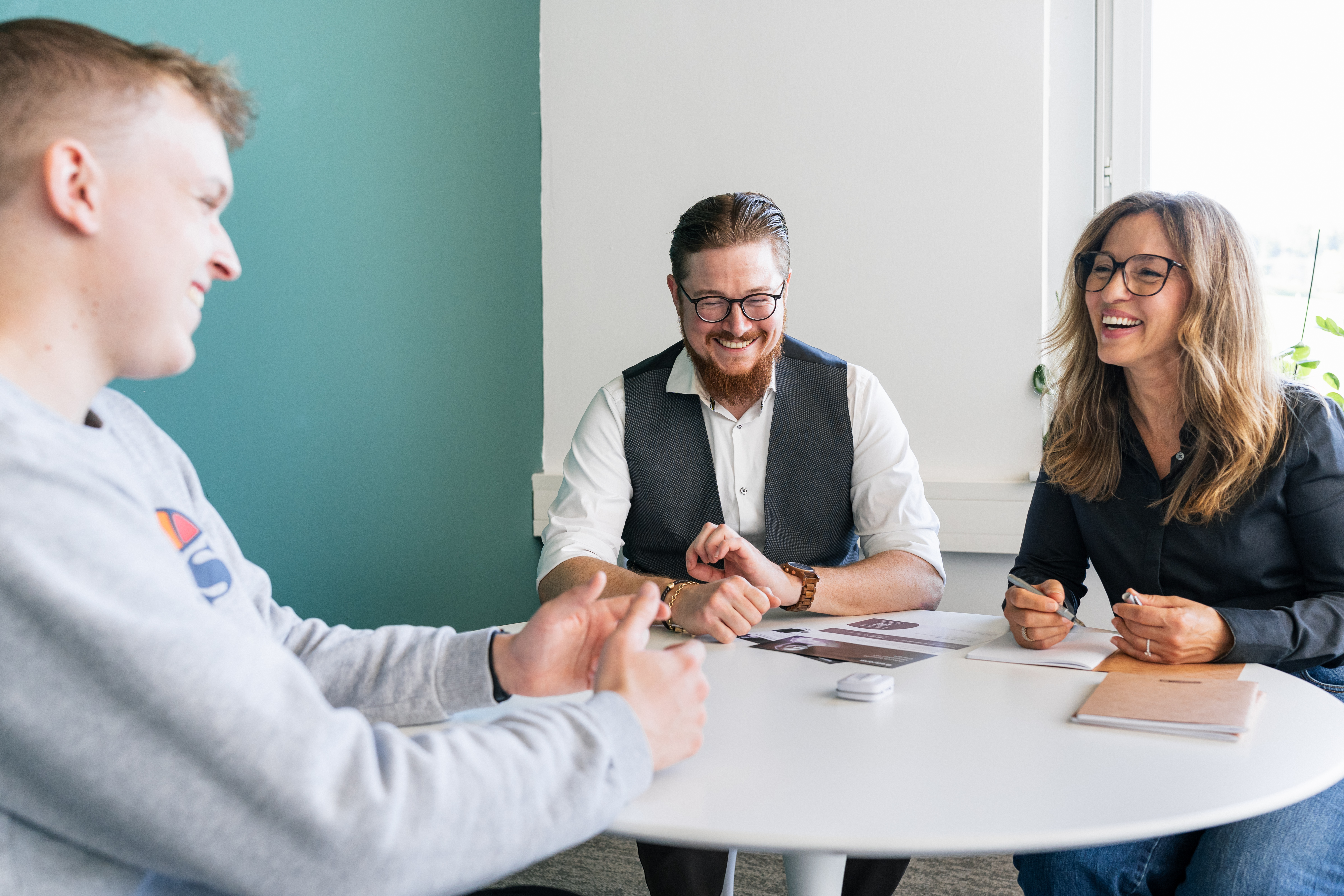 Drei Personen sitzen an einem Tisch und haben eine Besprechung